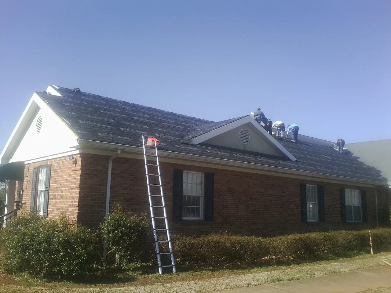 Crew tearing shingles off a brick ranch roof with a ladder set — Emergency Roof Repair work by our crew in Low Moor