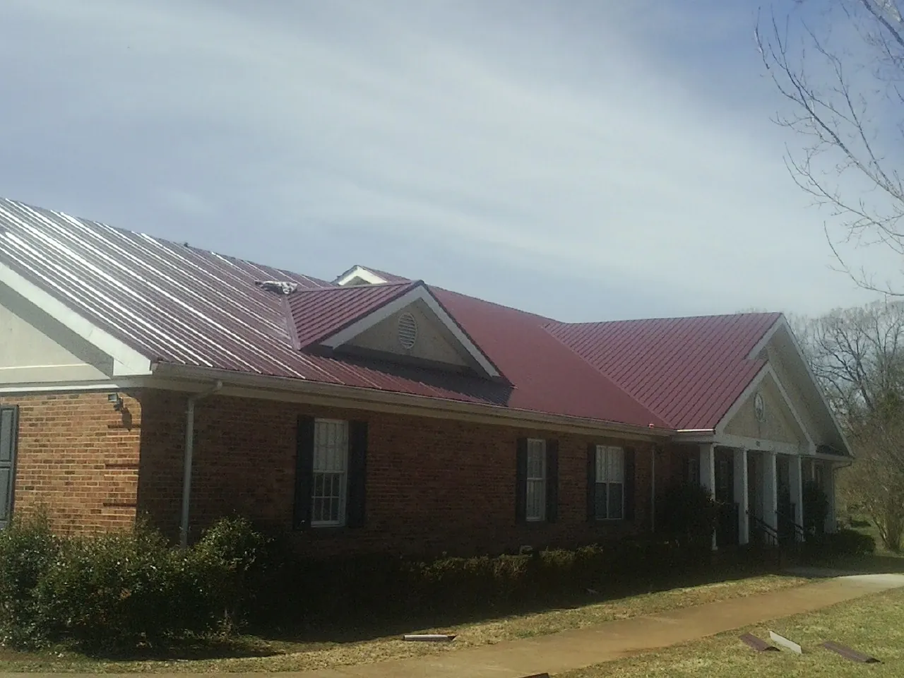 Red metal roof with gabled entries on a long brick building, from a Hail Damage Roof Repair job in Low Moor