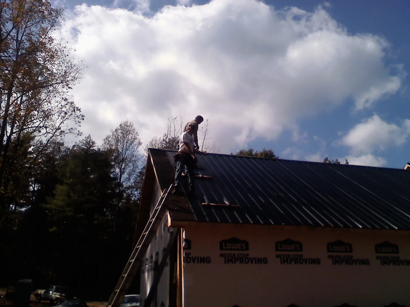 Roofer fastening dark metal panels high against a cloudy sky, from a Roof Inspection job in Low Moor